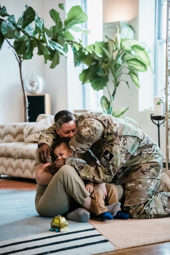 A soldier in uniform warmly embraces their family in a joyful homecoming moment.