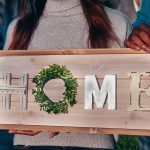 A couple holding a wooden sign spelling 'HOME' to celebrate their new residence.