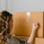 Back view of female in casual clothes writing fragile on empty side of carton box