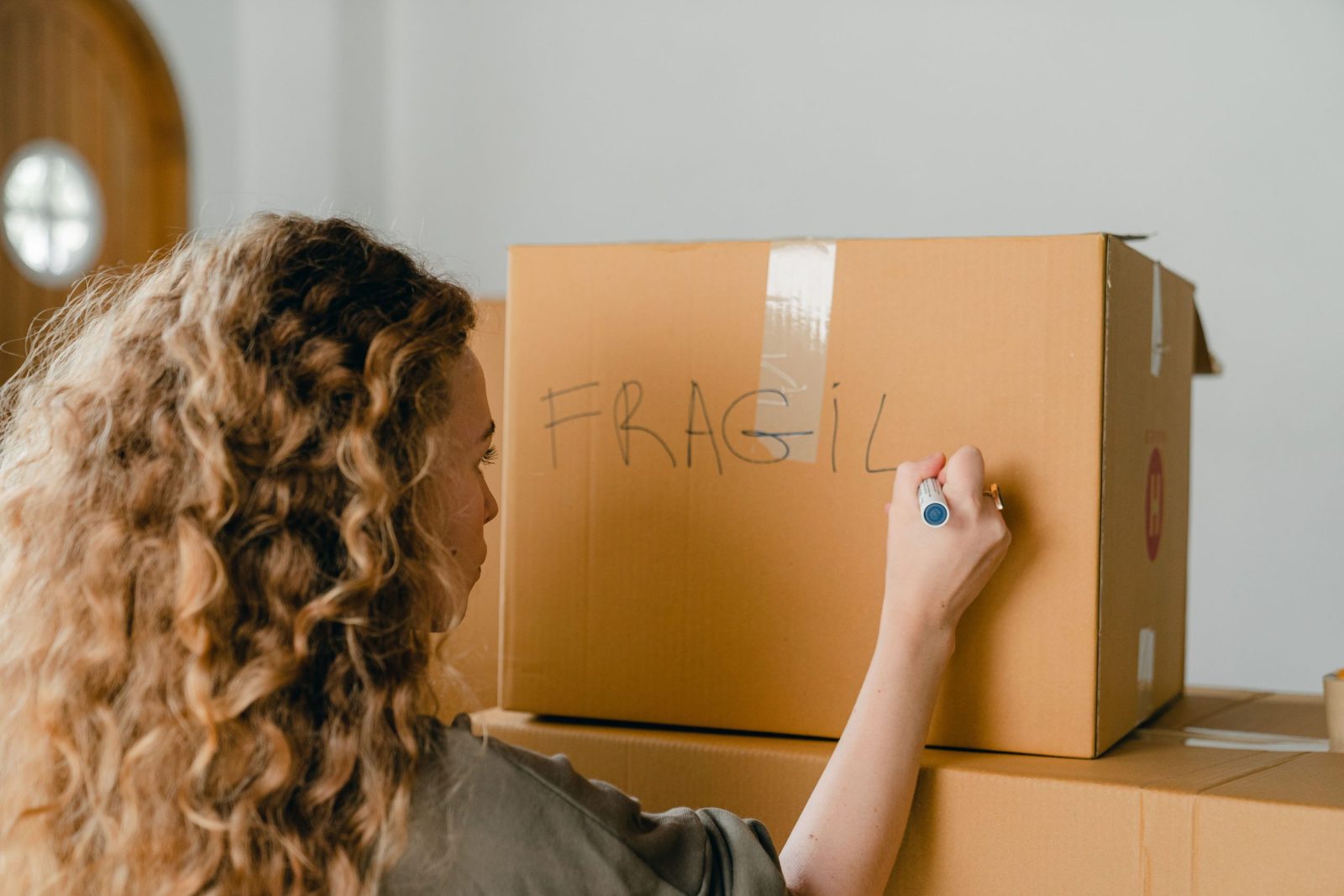 Back view of female in casual clothes writing fragile on empty side of carton box