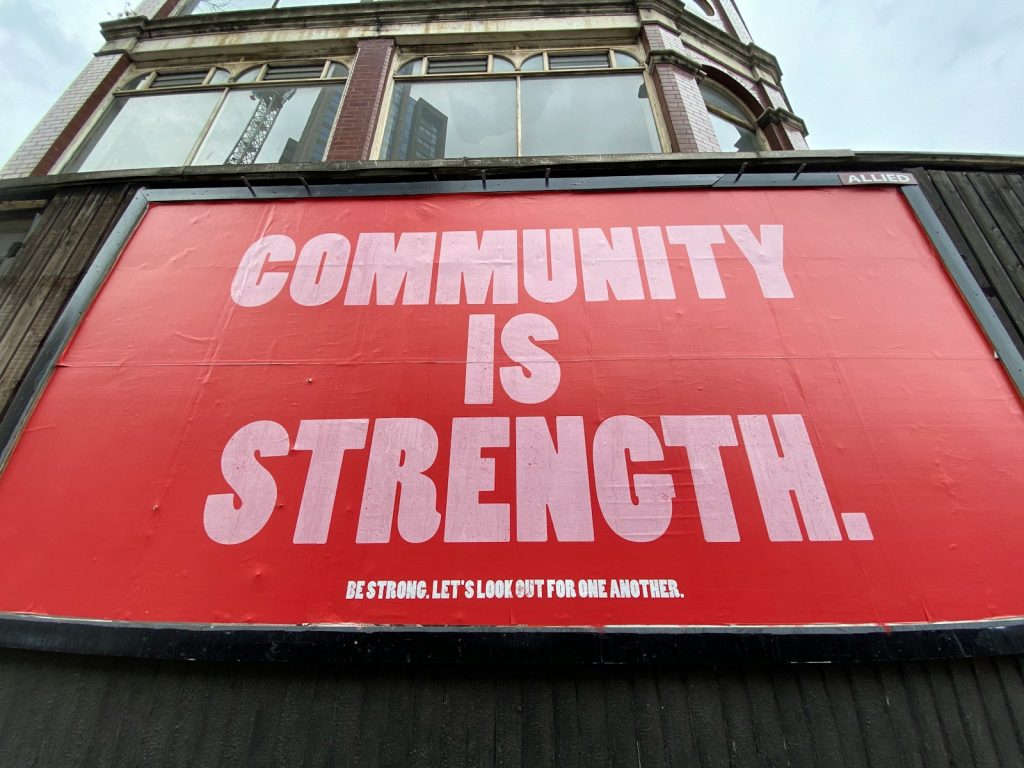 A large red billboard with white text reading COMMUNITY IS STRENGTH on a building